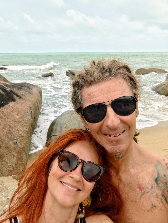 Seppi und Karin - Selfie am Strand. Im Hintergrund Felsen und Meer