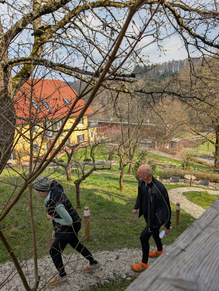 Babsi und Thomas gehen einen steilen Gartenweg bergauf. Im Hintergrund ein großes Wohnhaus