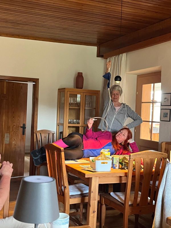 Karin liegt mit Einlaufgerät am Tisch, Babsi steht dahinter und hält den Wasserbehälter nach oben.