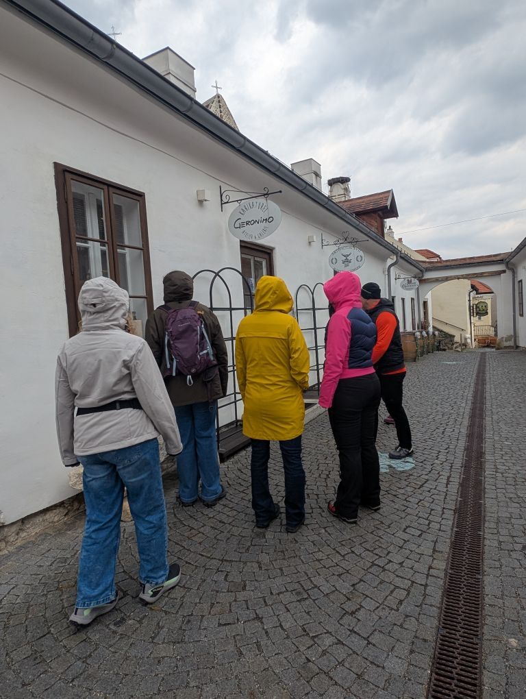 Fünf bunt gekleidete Menschen mit Kapuzen in einer netten Gasse, bei trübem Wetter.