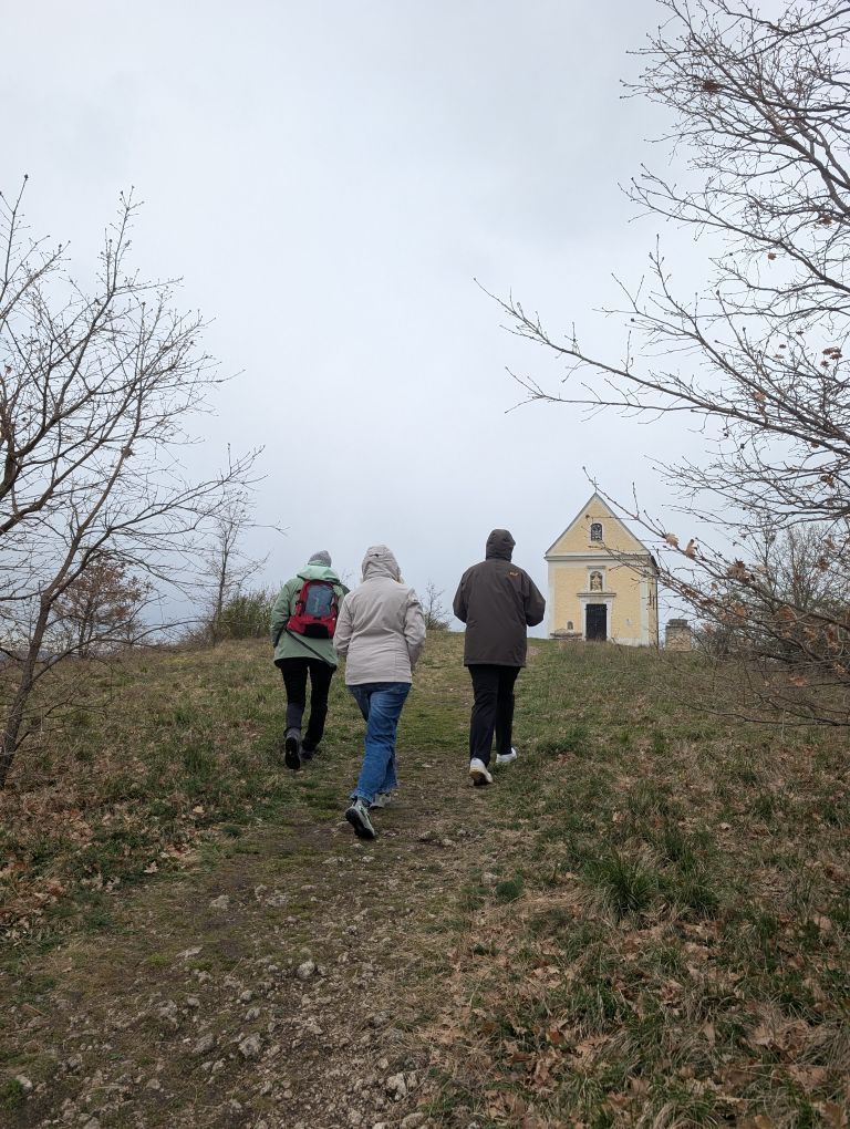 Der Frauen von hinten, wie sie über eine ansteigende Wiese auf eine Kapelle zugehen.