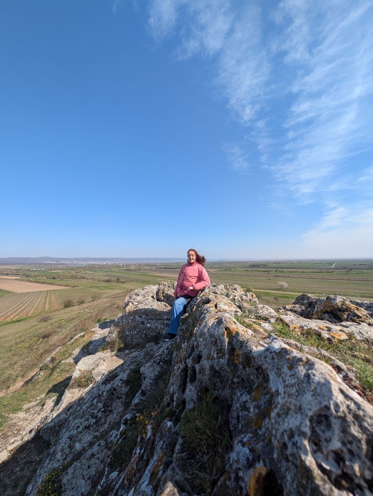 Frau sitzend auf einem Felsen mit traumhaftem Weitblick auf die umliegende weite, grüne Landschaft.