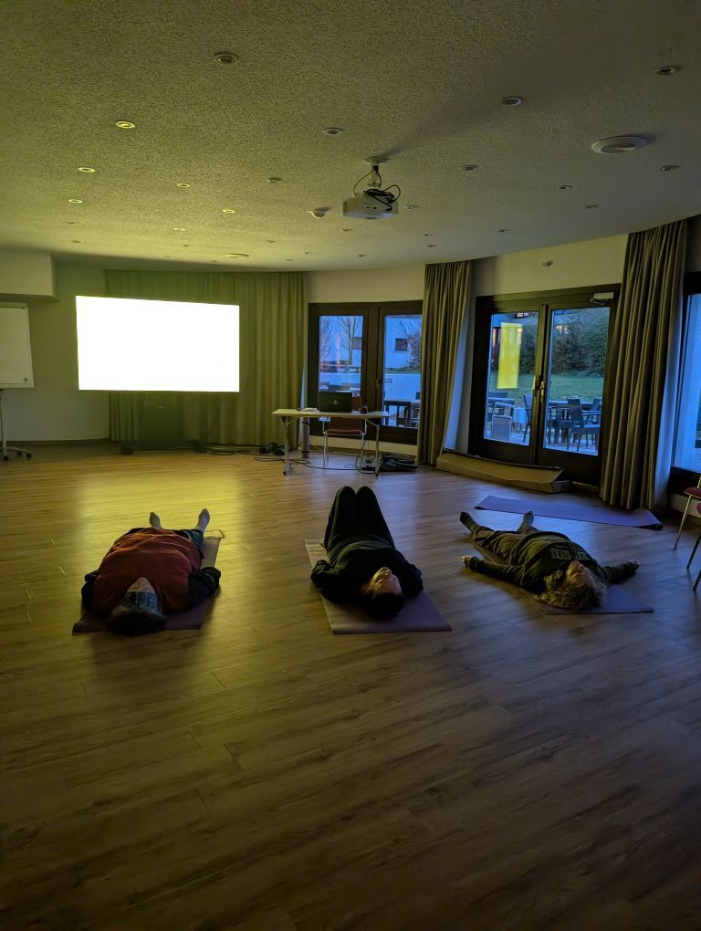 3 Frauen liegen in einem dunklen Raum auf Matten am Boden