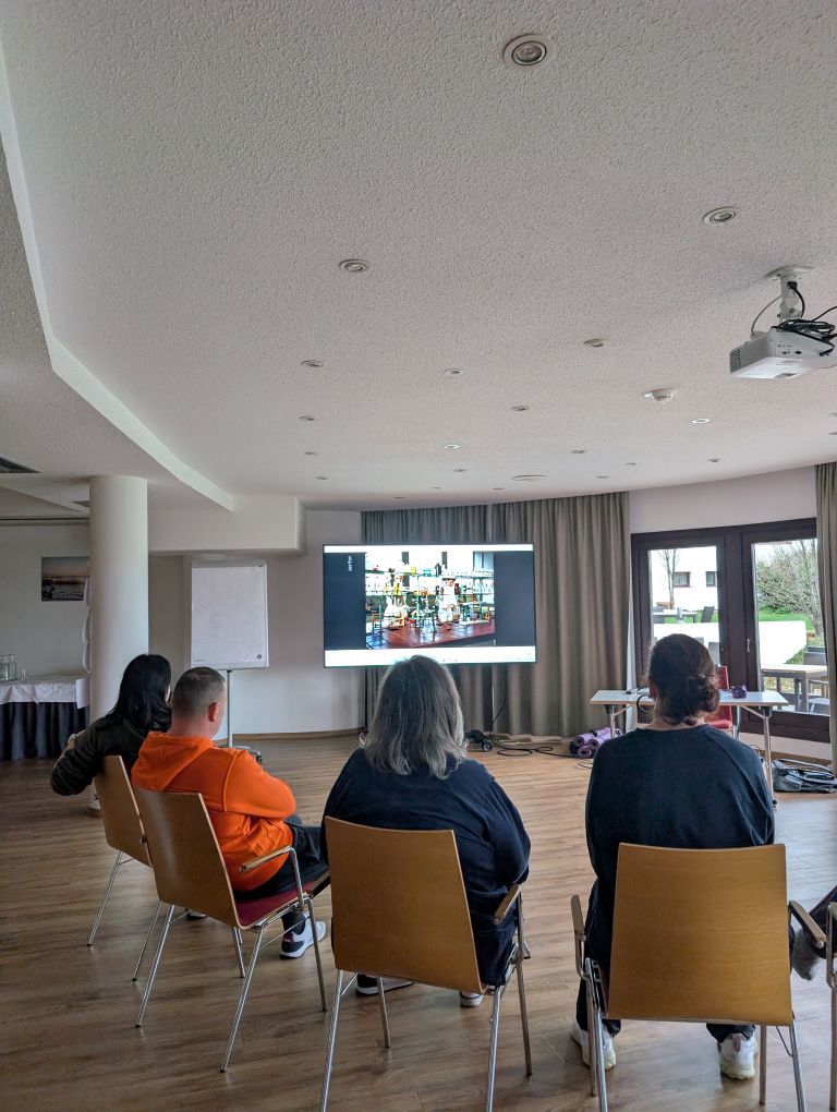 4 sitzende Menschen von hinten, wie sie auf einen großen Bildschirm schauen