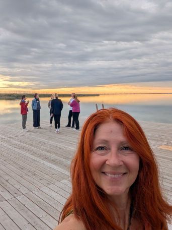 Karin Selfie am Steg, im Hintergrund die ersten Teilnehmer und der Sonnenaufgang am See
