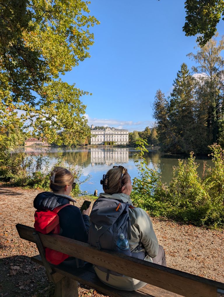 Zwei Teilnehmerinnen von hinten, sitzend auf eine Bank, und auf den Leopoldskroner Weiher blickend