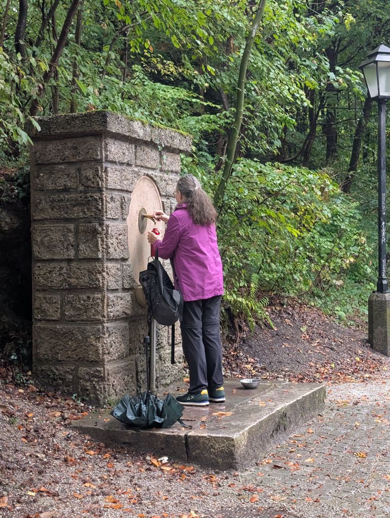 Christina füllt ihre Trinkflasche beim Brunnen am Wegesrand